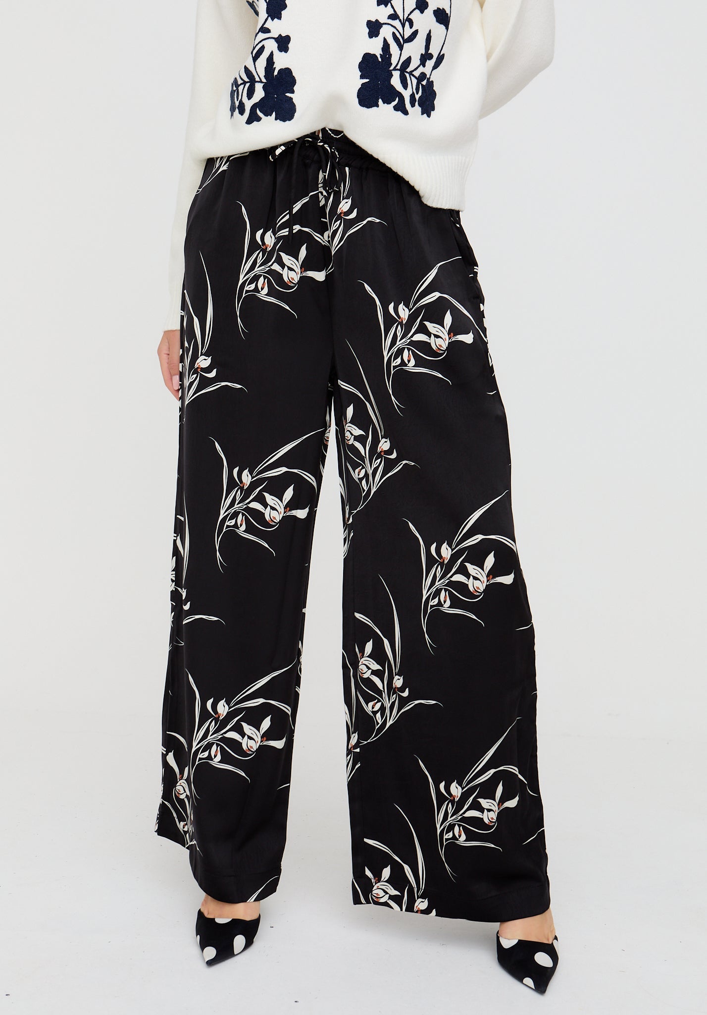 Black floral-patterned pants worn by a person on a white background