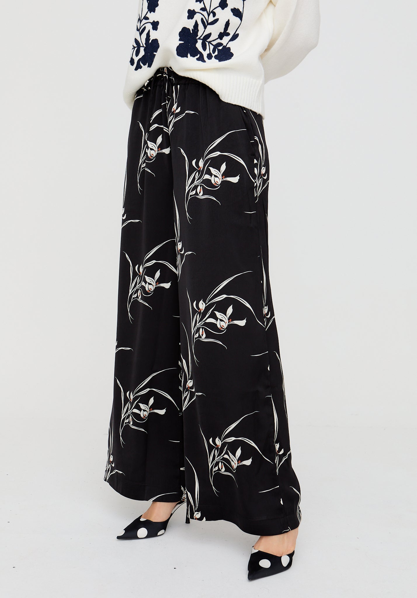Black floral-patterned pants worn by a person on a white background