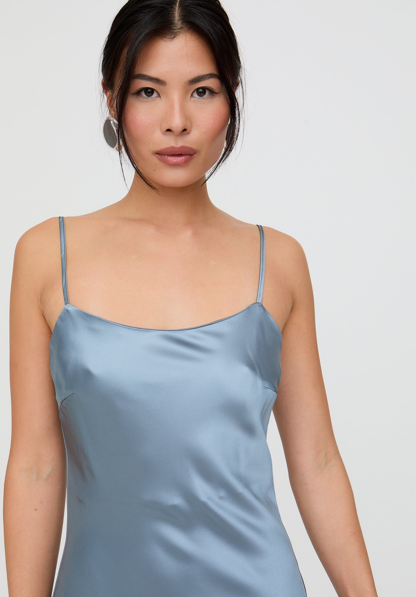 Woman wearing a light blue satin slip dress against a plain background