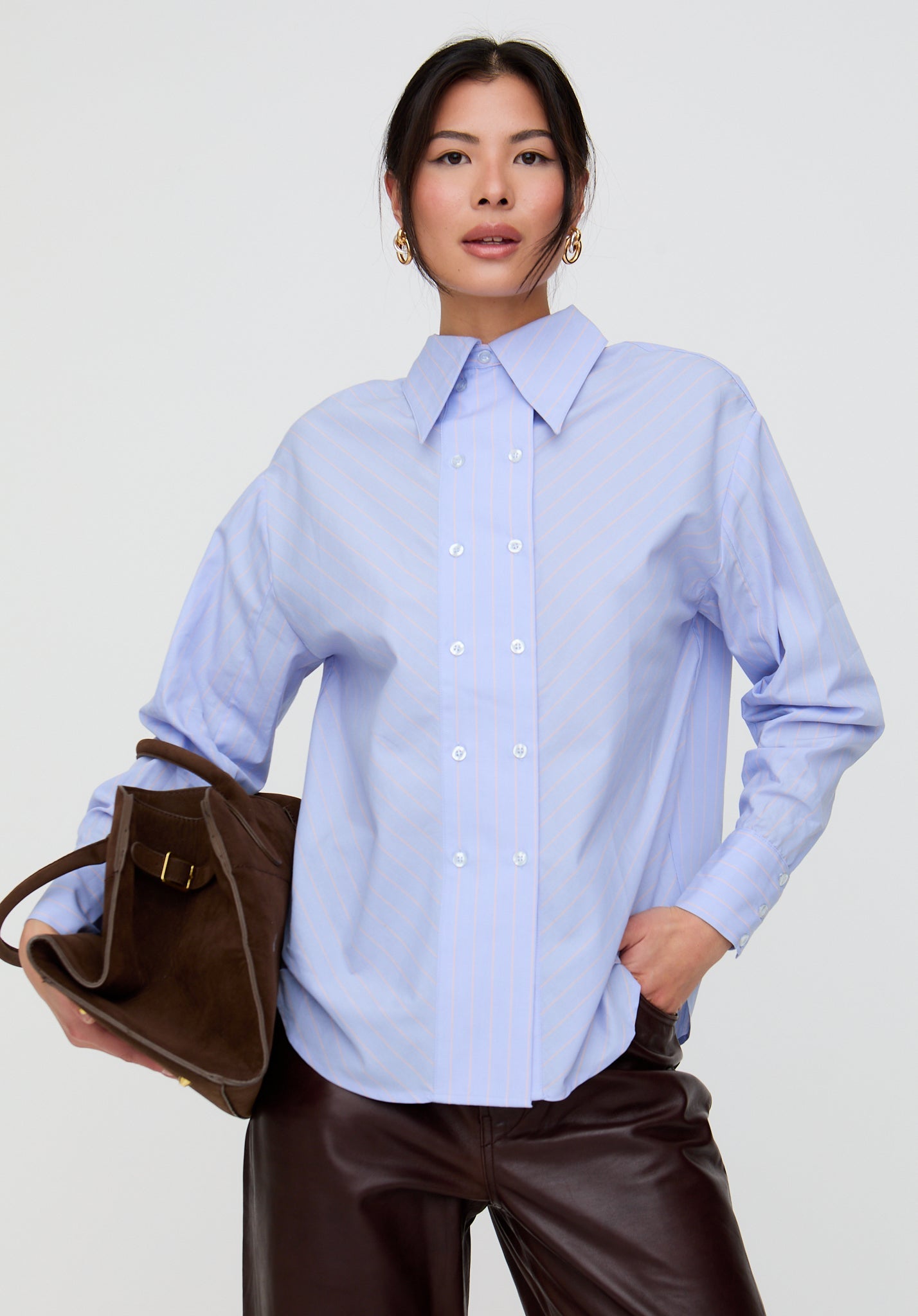 Woman wearing a light blue shirt and holding a brown bag on a white background