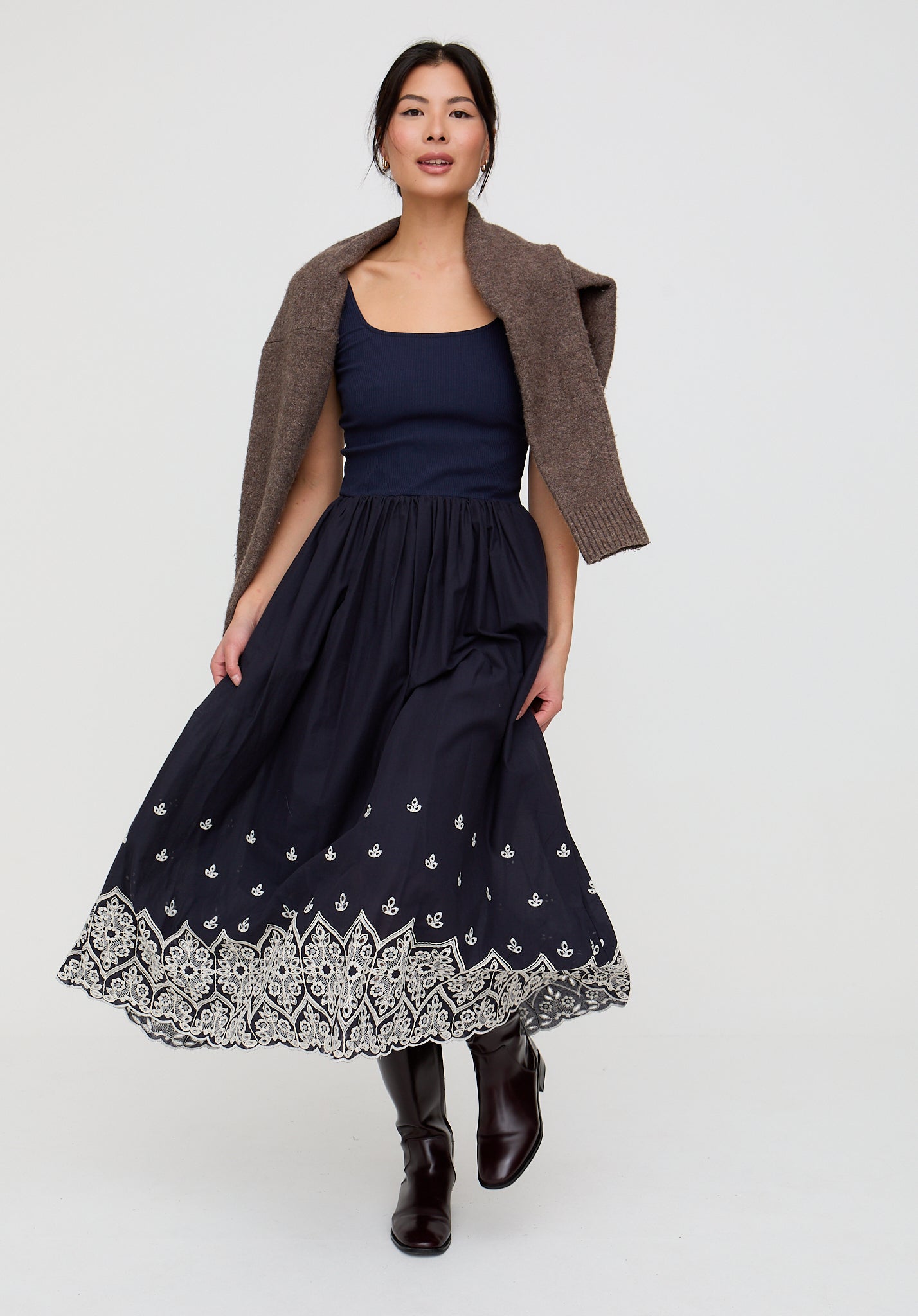 Woman wearing a navy dress with a patterned hem and brown cardigan on a white background
