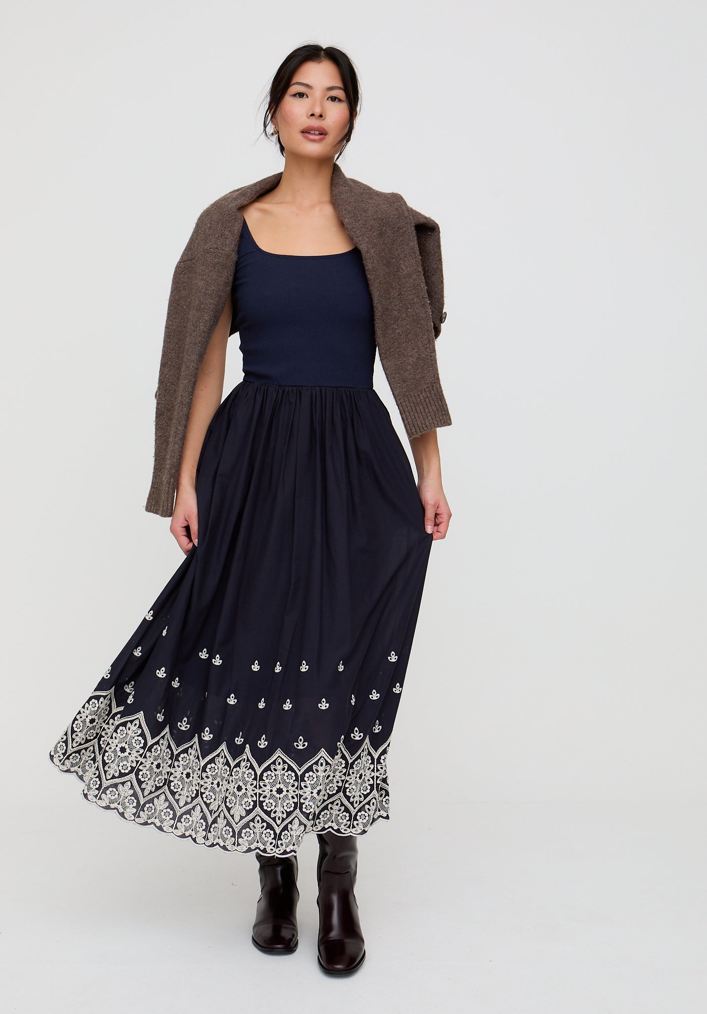 Woman wearing a navy dress with a patterned hem and brown cardigan on a white background