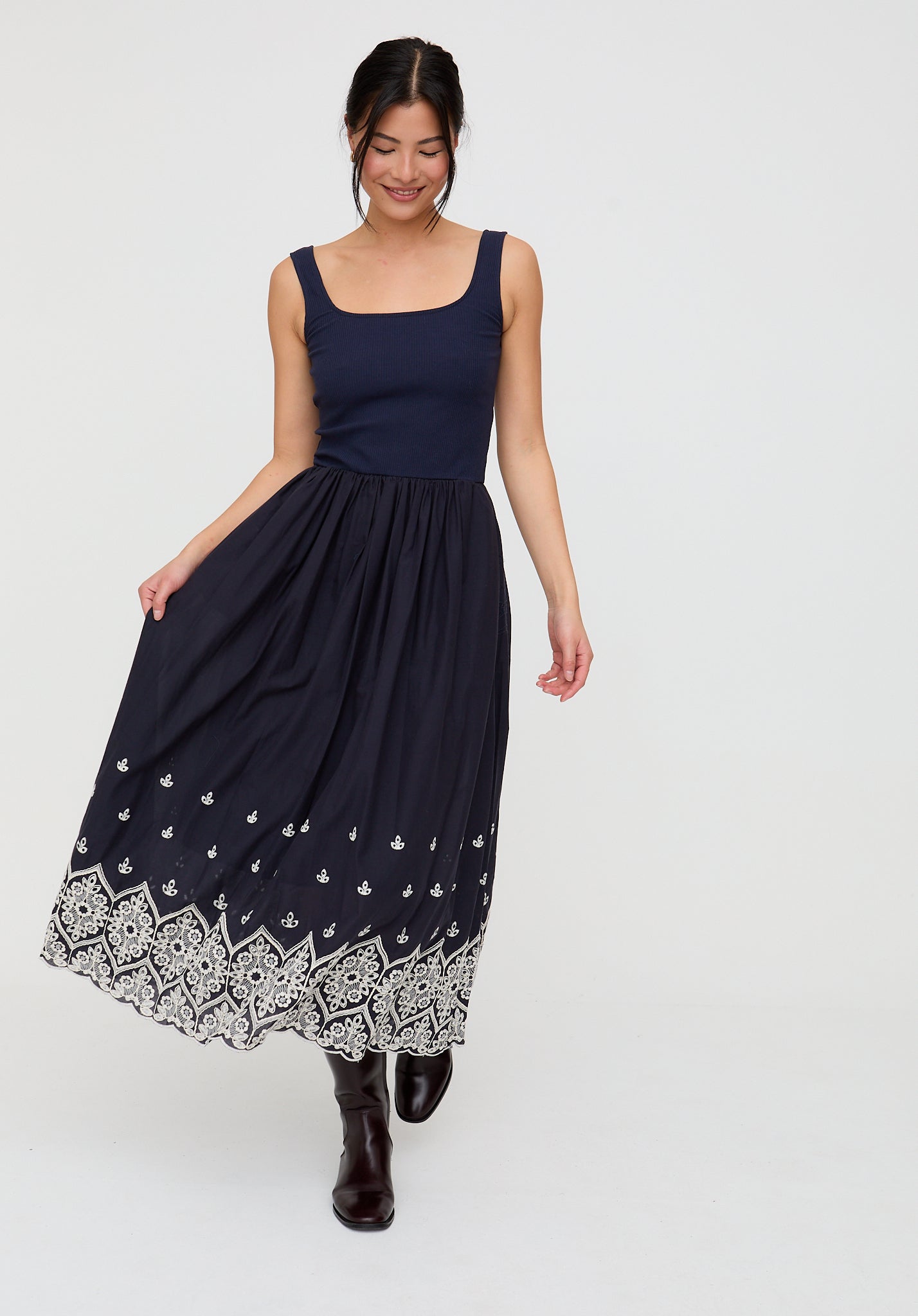 Woman wearing a navy dress with white patterned hem on a white background