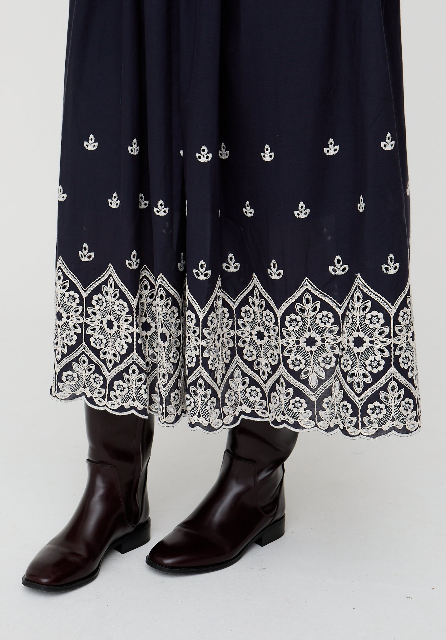 Navy blue dress with white embroidery and brown boots on a white background
