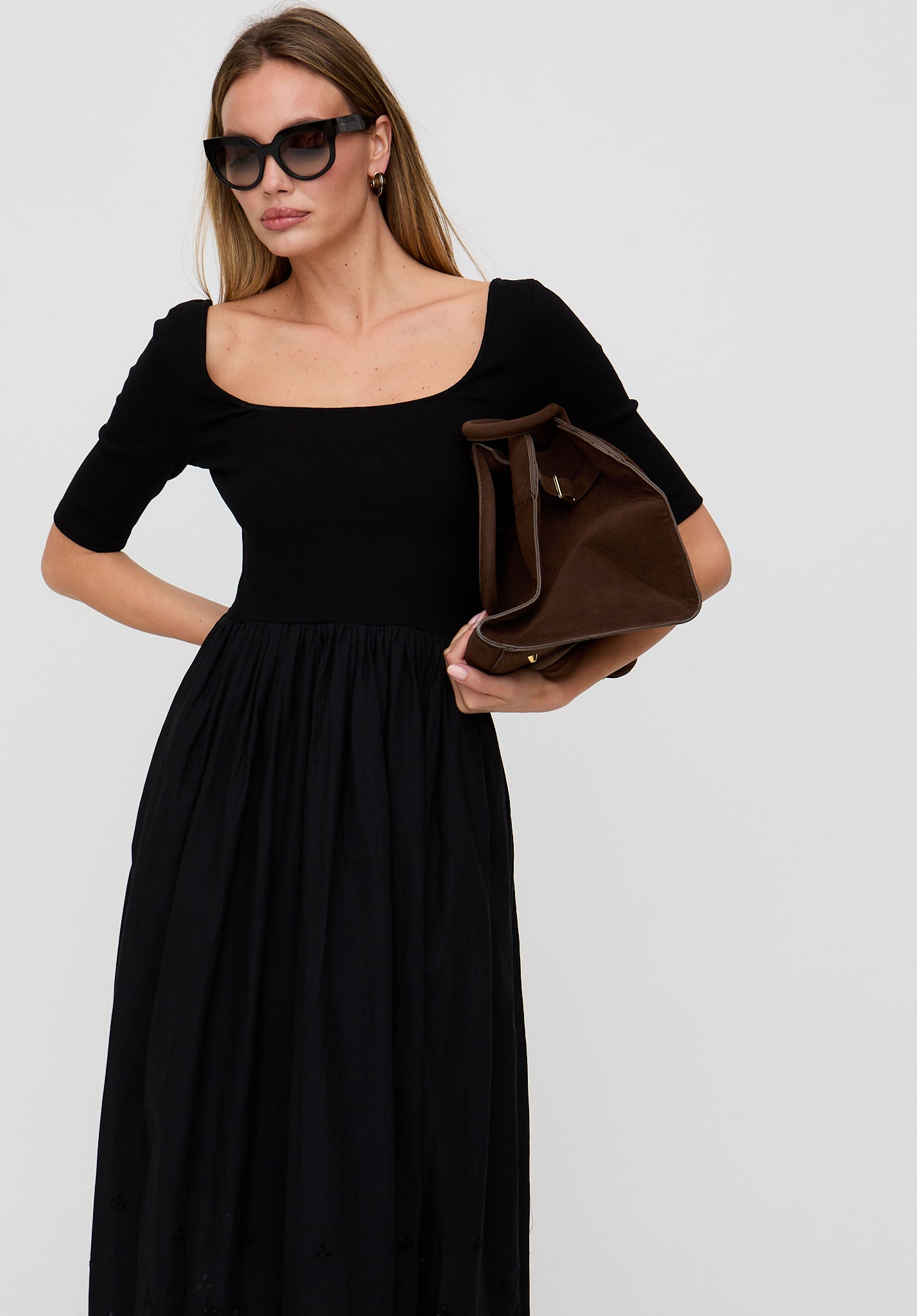 Woman wearing a black dress holding a brown bag against a white background