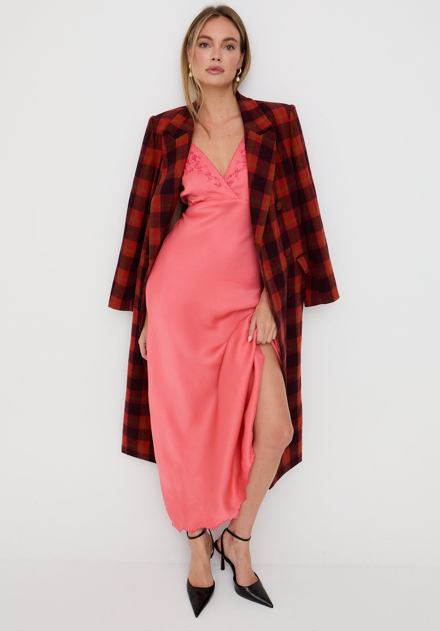 Woman wearing a pink dress with a red plaid coat on a white background