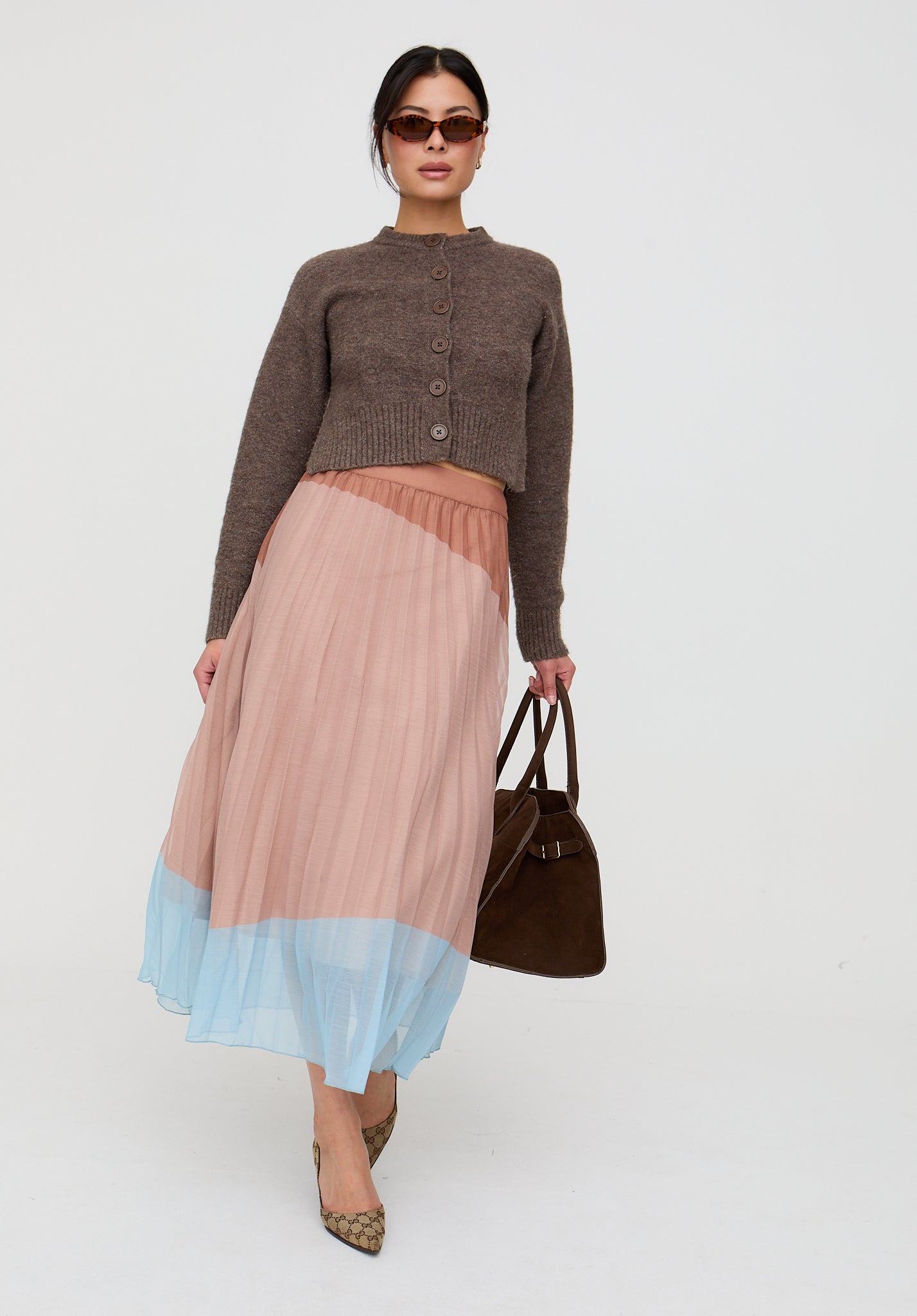 Woman wearing a brown cardigan and a two-tone skirt with a plain background