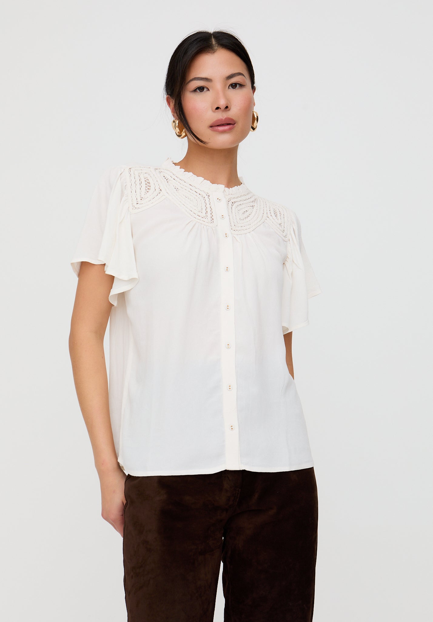 Woman wearing a white blouse with floral details on a plain background