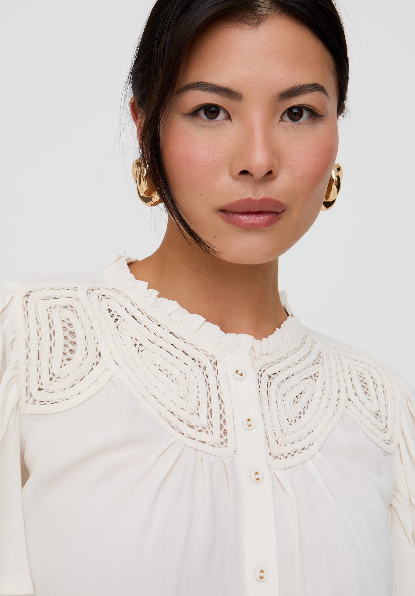 Woman wearing a white blouse with intricate lace detailing on a plain background