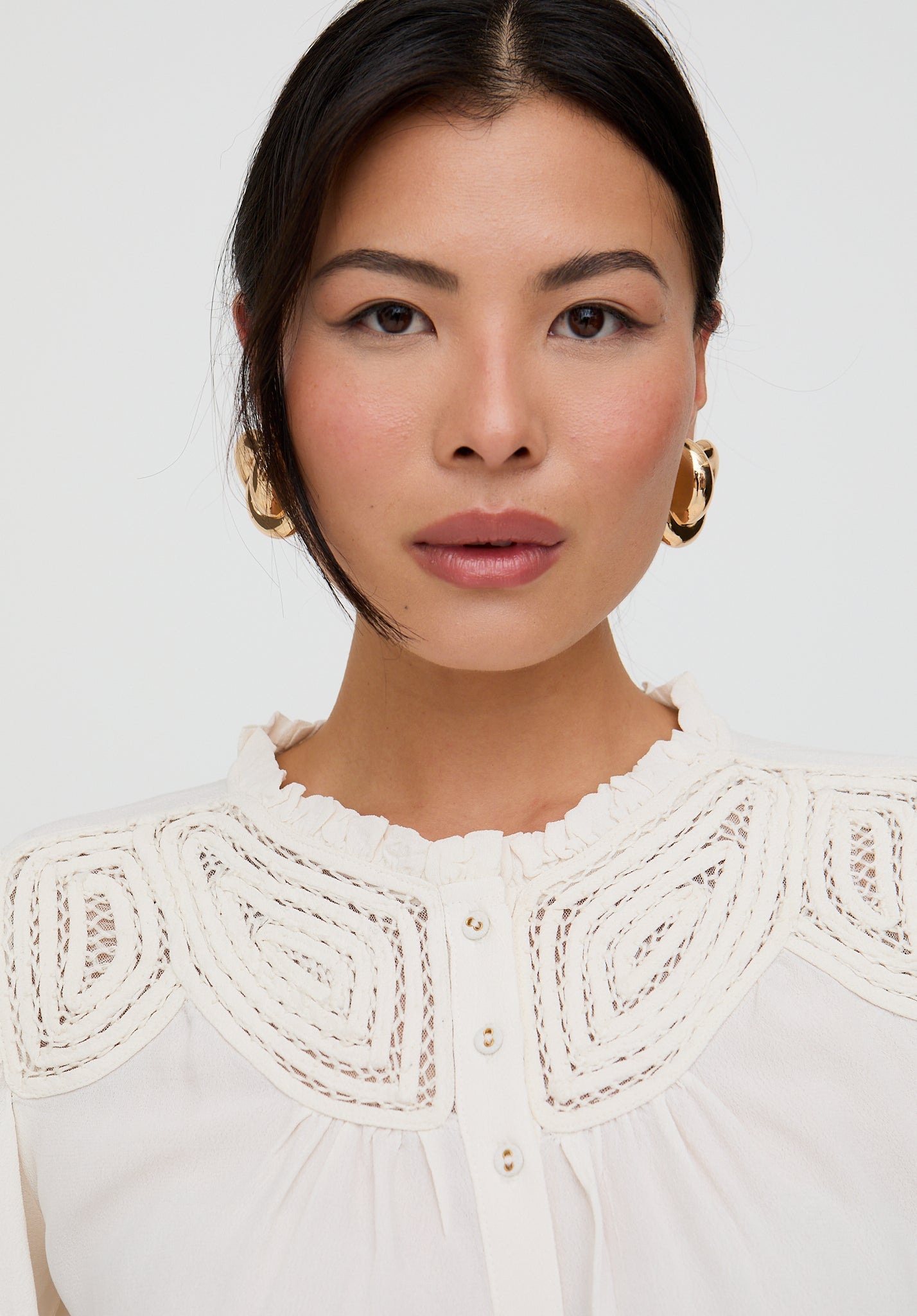 Woman wearing a white blouse with intricate lace detailing on a plain background