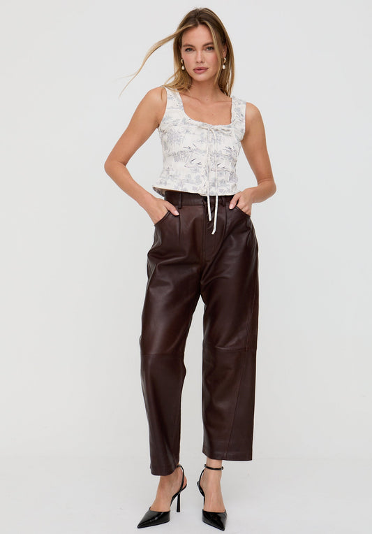 Woman wearing a white lace top and brown leather pants on a white background