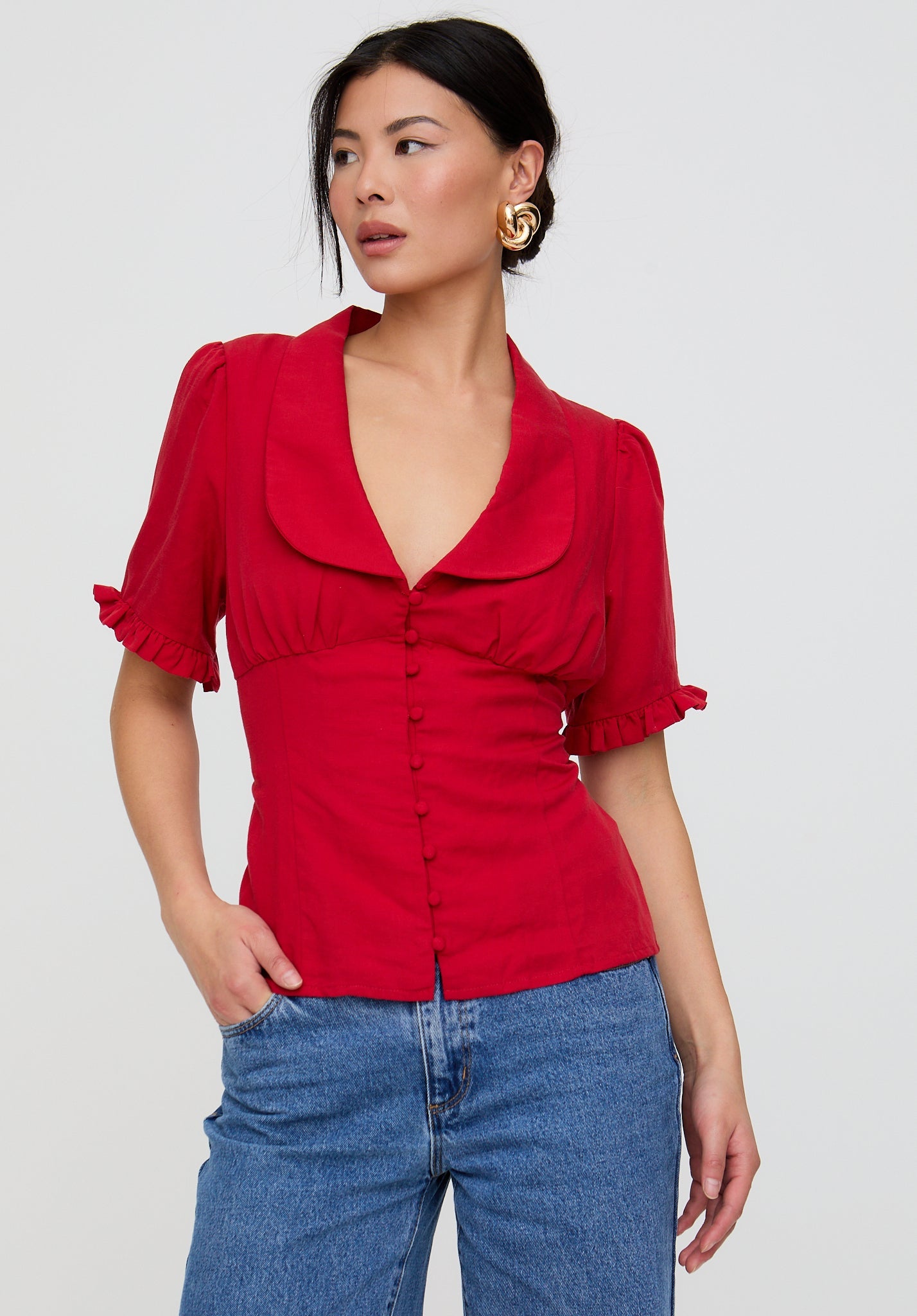 Woman wearing a red blouse with puffed sleeves and blue jeans on a white background