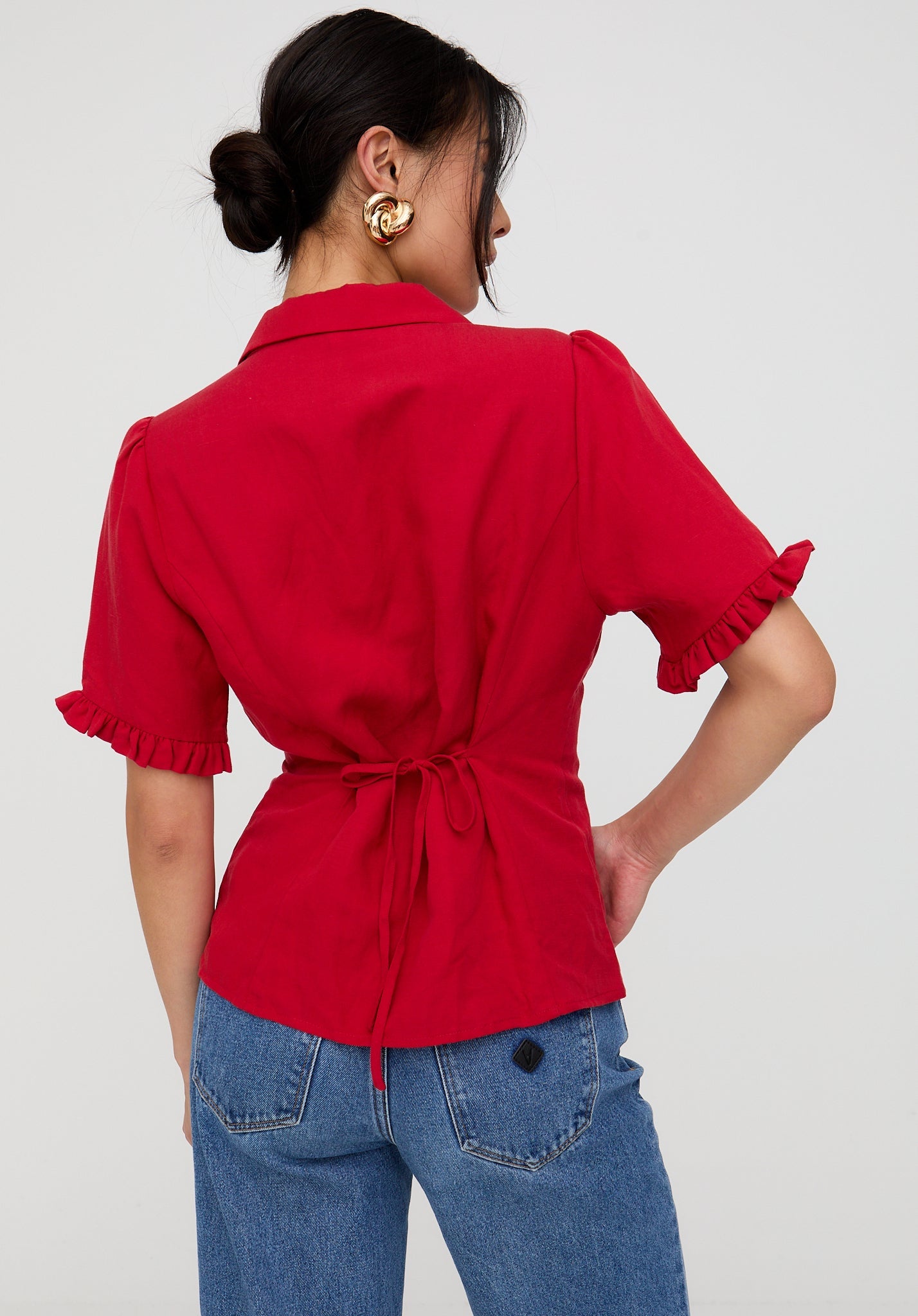 Person wearing a red blouse with ruffled sleeves and blue jeans on a white background