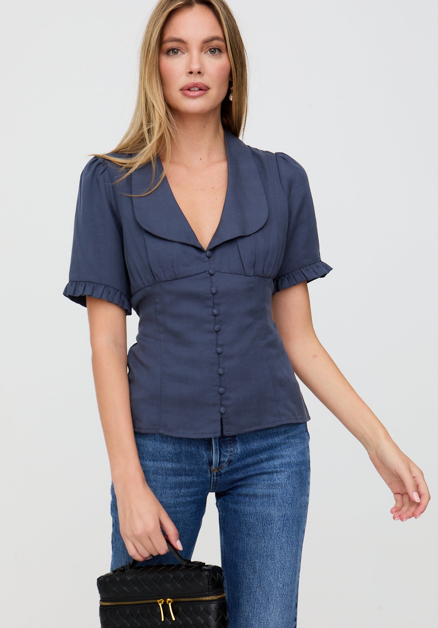 Woman wearing a navy blue blouse with ruffled sleeves and jeans on a white background